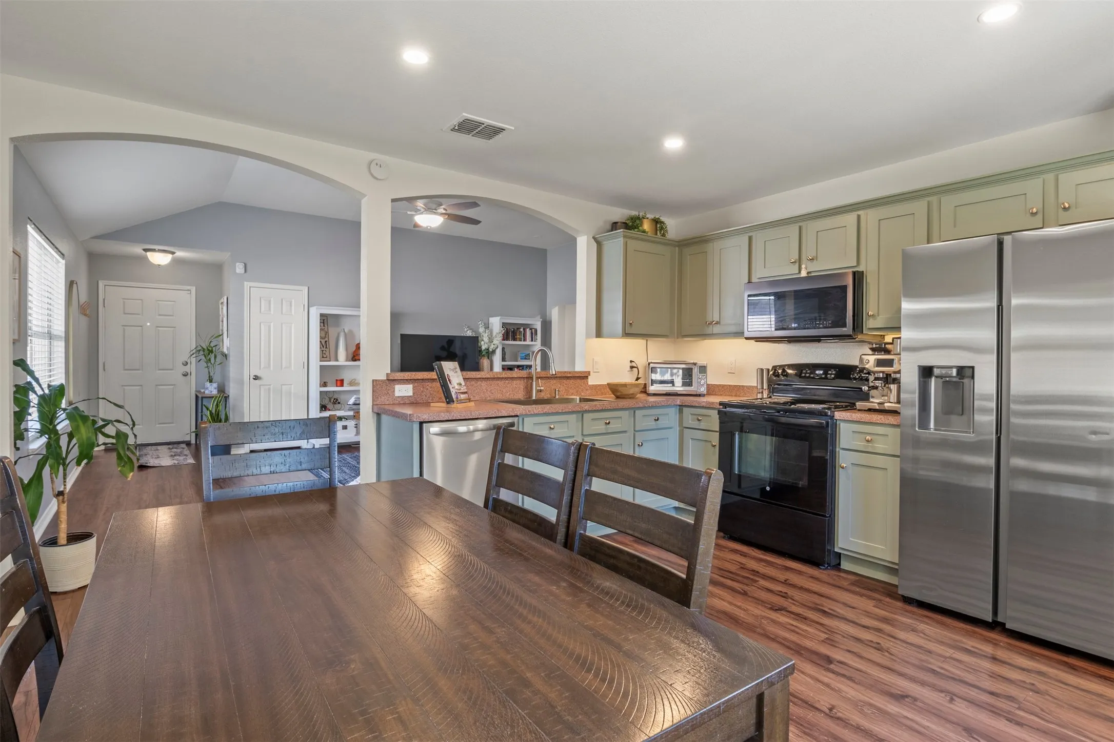 Kitchen featuring wood-finish flooring, recessed lighting, stainless steel refrigerator, black range, and sage-finish cabinetry