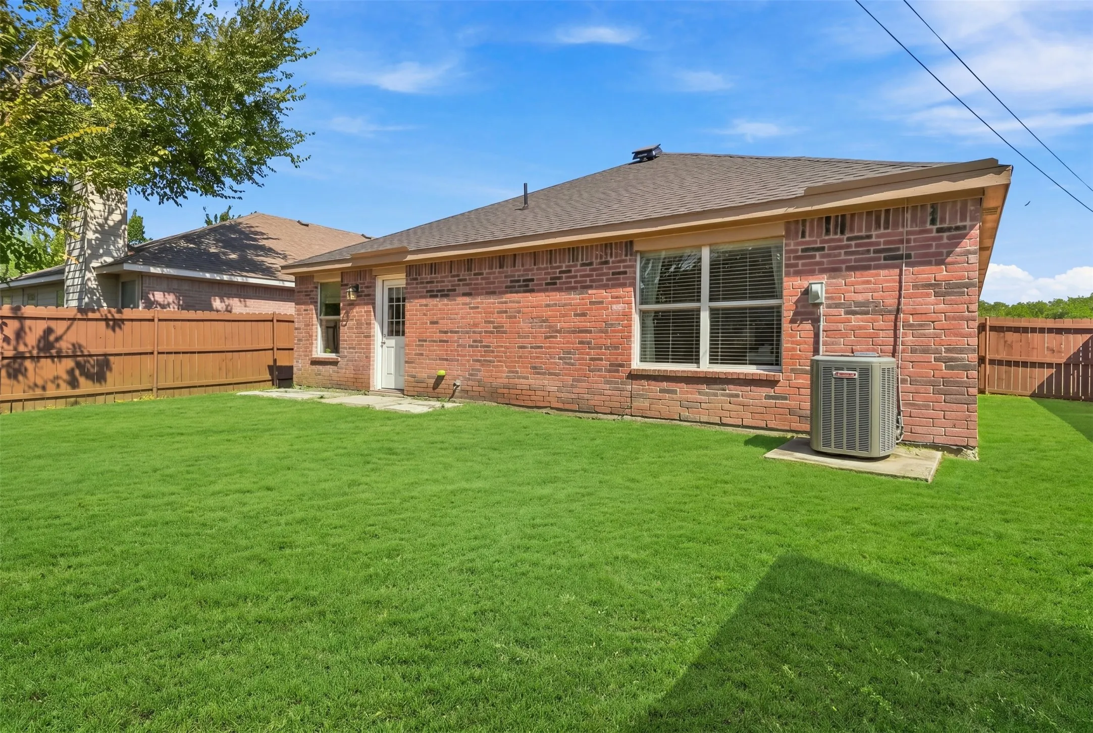 Expansive backyard featuring a manicured lawn, brick exterior, and a privacy fence