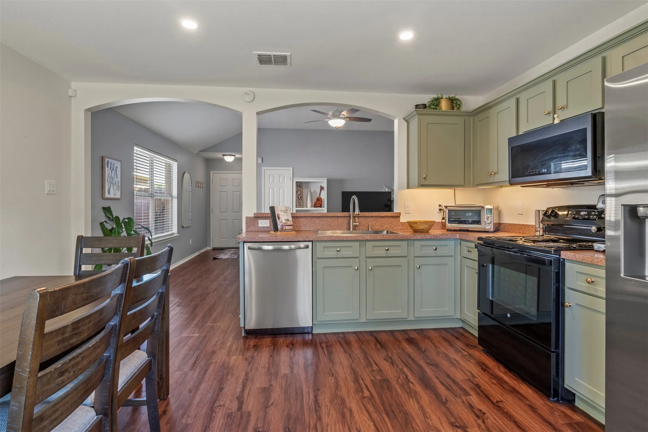 Kitchen featuring olive-toned cabinetry, stainless steel dishwasher, black range, and wood-finish flooring