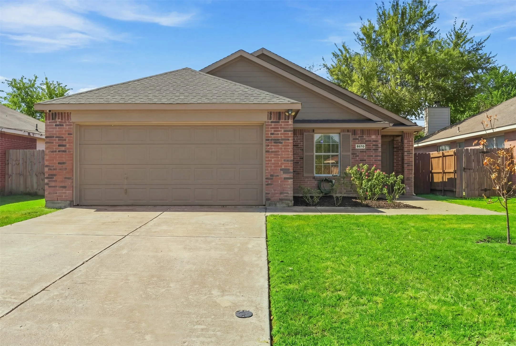 Red brick exterior with a two-car garage, concrete driveway, and front lawn