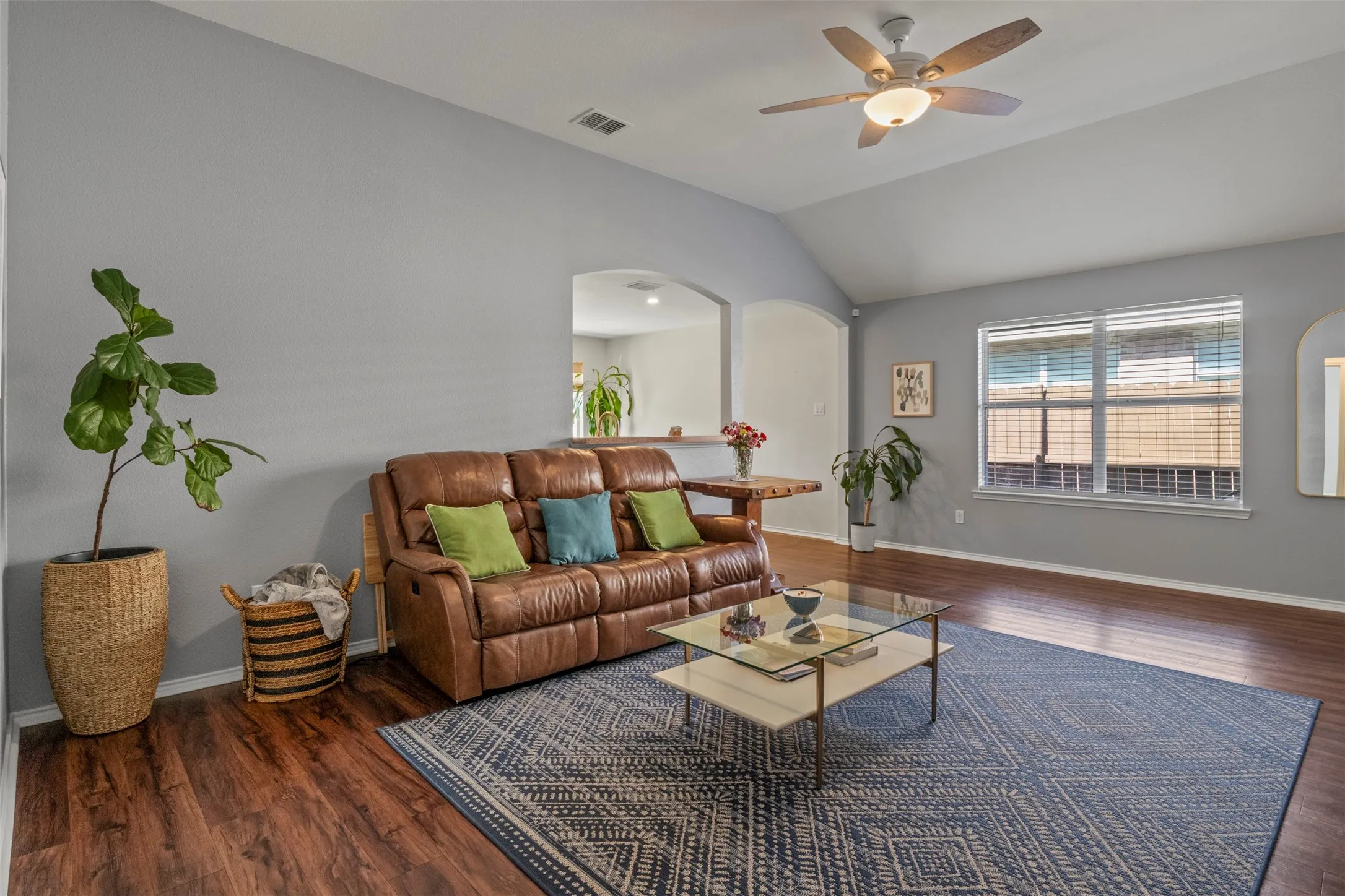 Vaulted ceiling with a ceiling fan, wood-finish flooring, and multiple windows