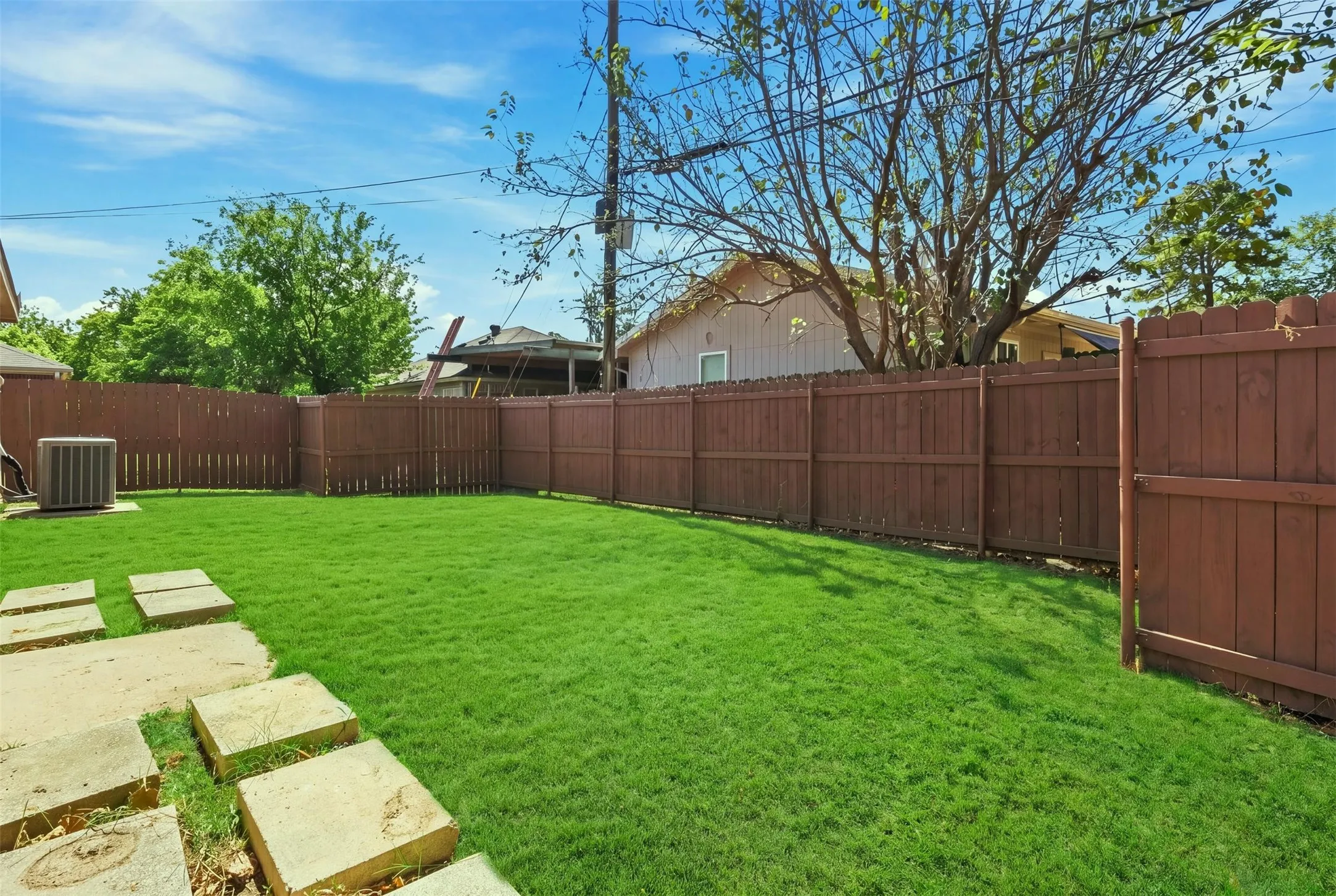 Expansive backyard featuring a manicured lawn, full perimeter wood fencing, and concrete stepping stones