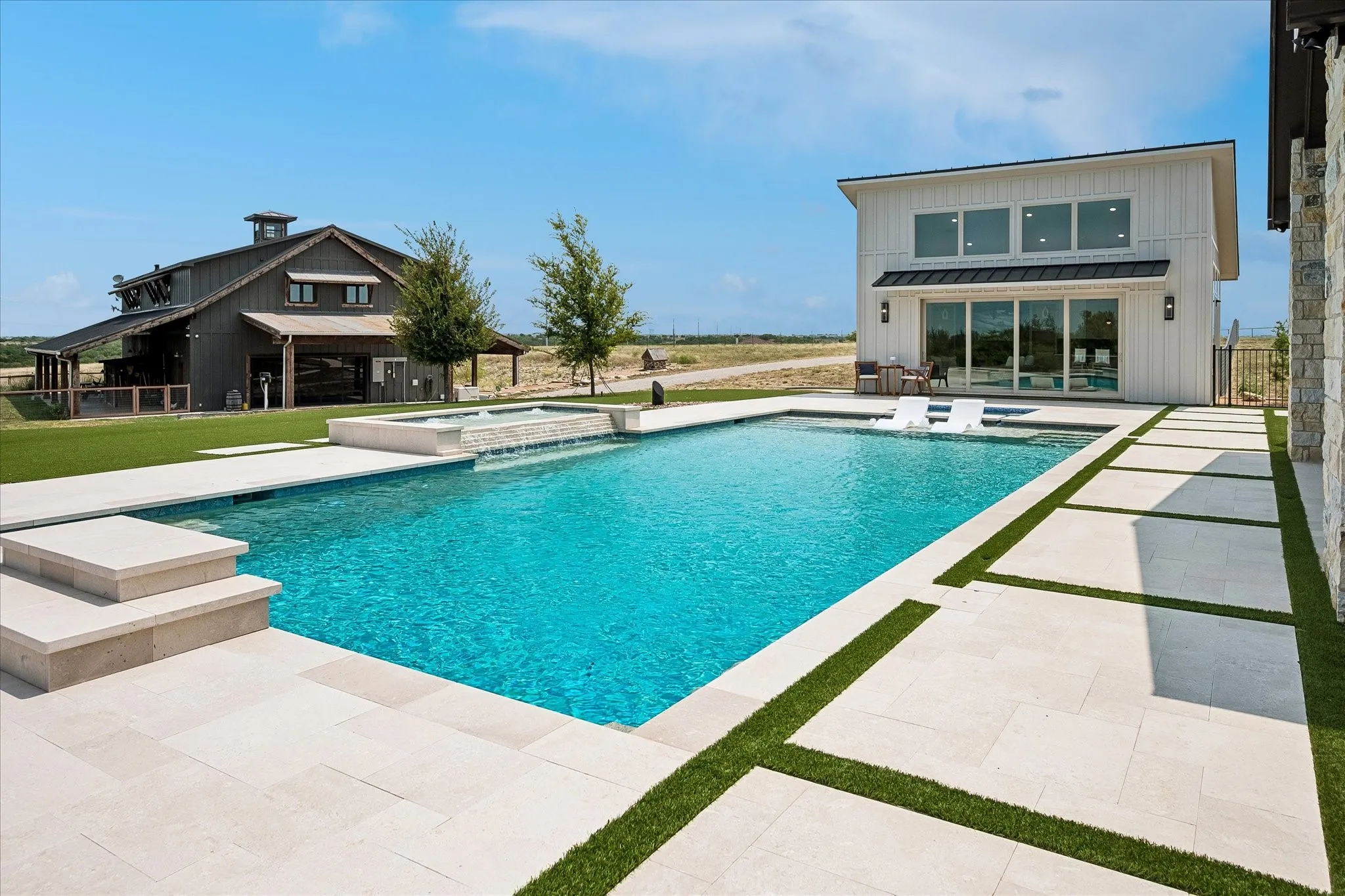 Contemporary pool styling with water feature, adjoining hot tub and partially submerged lounge chairs.