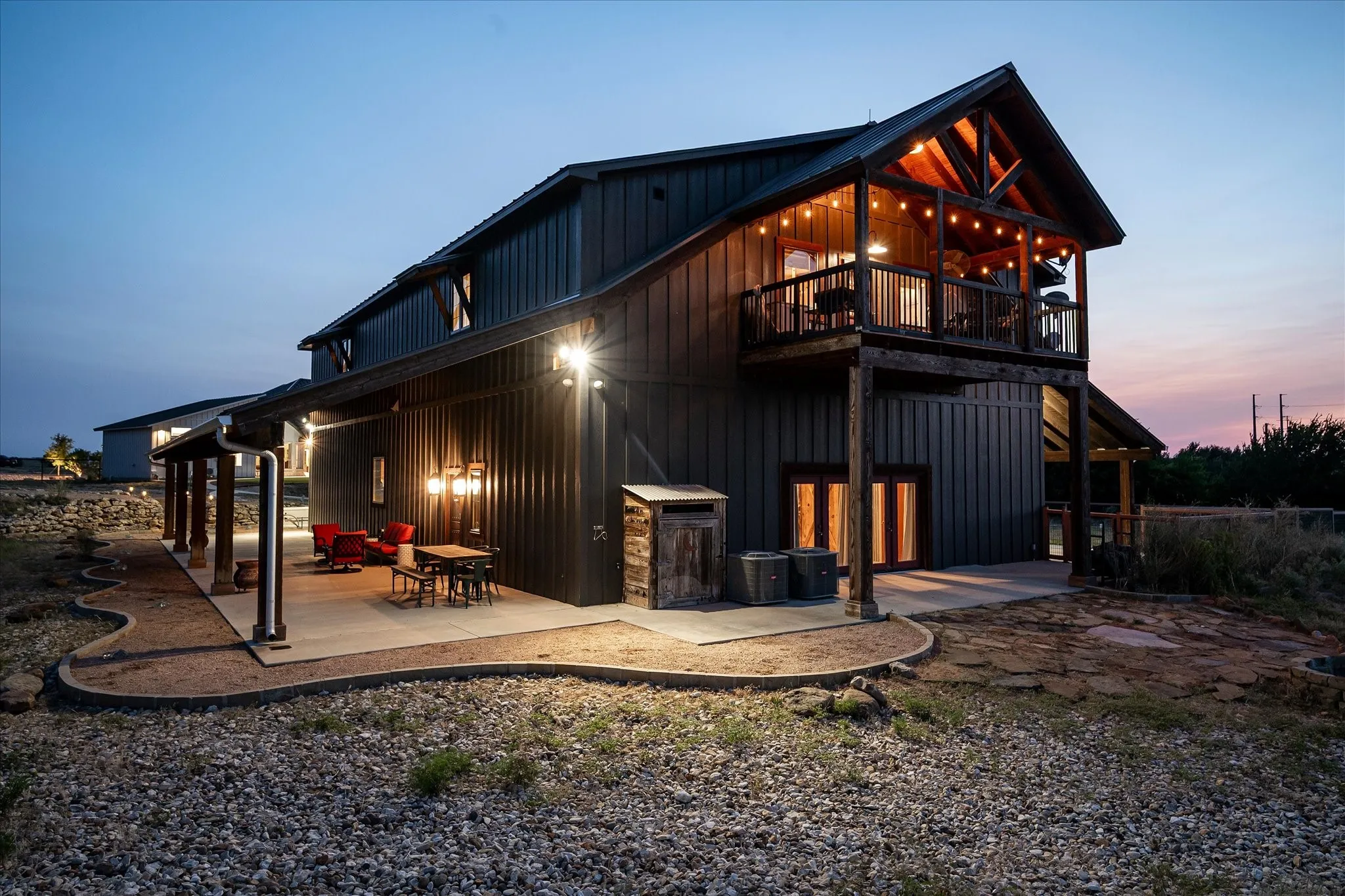 Side view of the Barndominium at dusk. Beautiful views of Lake Benbrook and spectacular Texas sunsets from the porch upstairs. Hard to see in this picture but there is a galvanized corrugated steel roof accent on the side elevations. Barn also has a large stone firepit and private driveway.