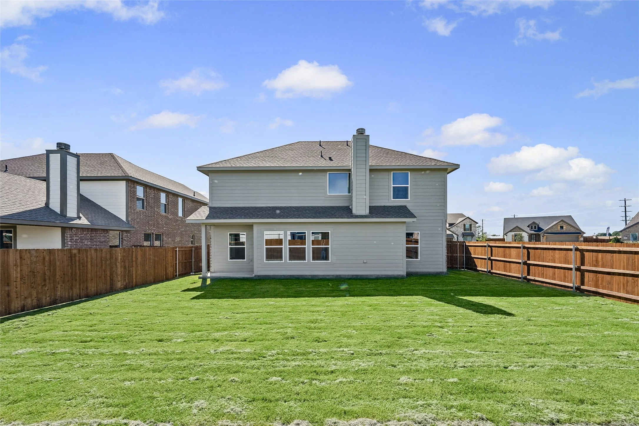 Expansive backyard with a manicured lawn, full wood fencing, and a two-story residence featuring siding and a prominent chimney