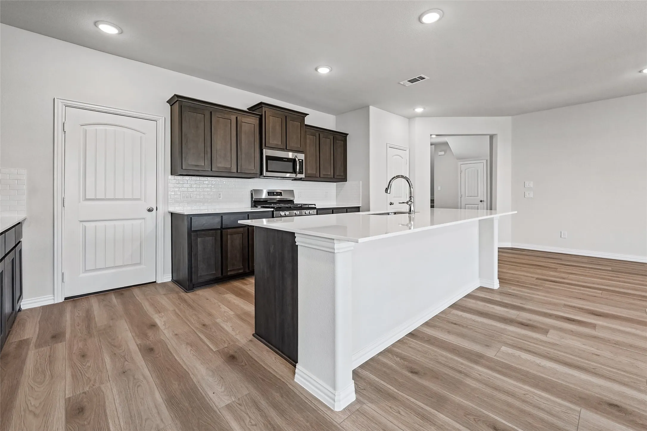 Kitchen featuring a large island with white countertop, dark wood-finish cabinetry, stainless steel appliances, white subway tile backsplash, and wood-finish flooring