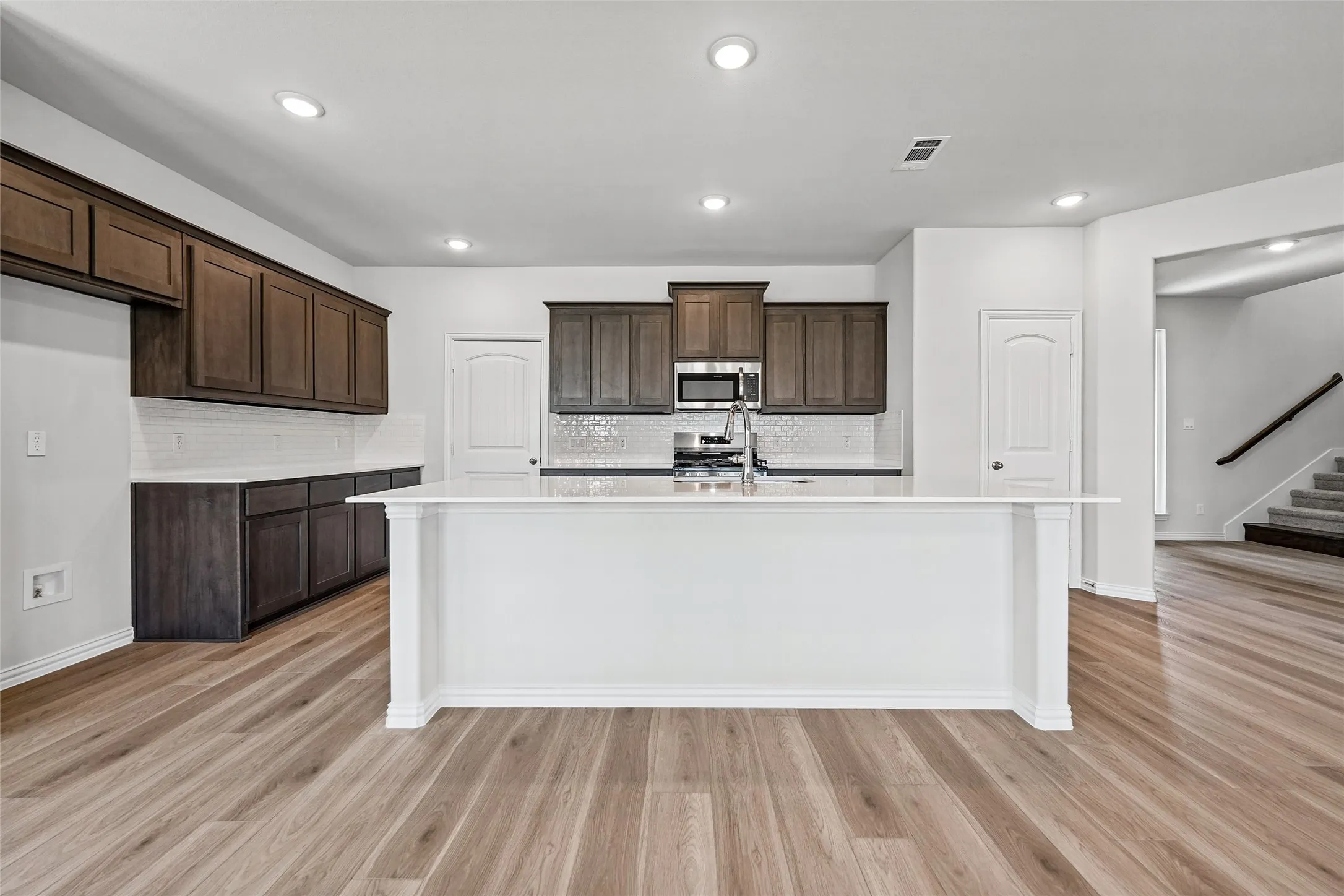 Modern kitchen and open living area featuring rich wood-finish cabinetry, stainless steel appliances, quartz countertops, a large center island with white base, recessed ceiling lighting, and wide-plank wood-finish flooring throughout the main level