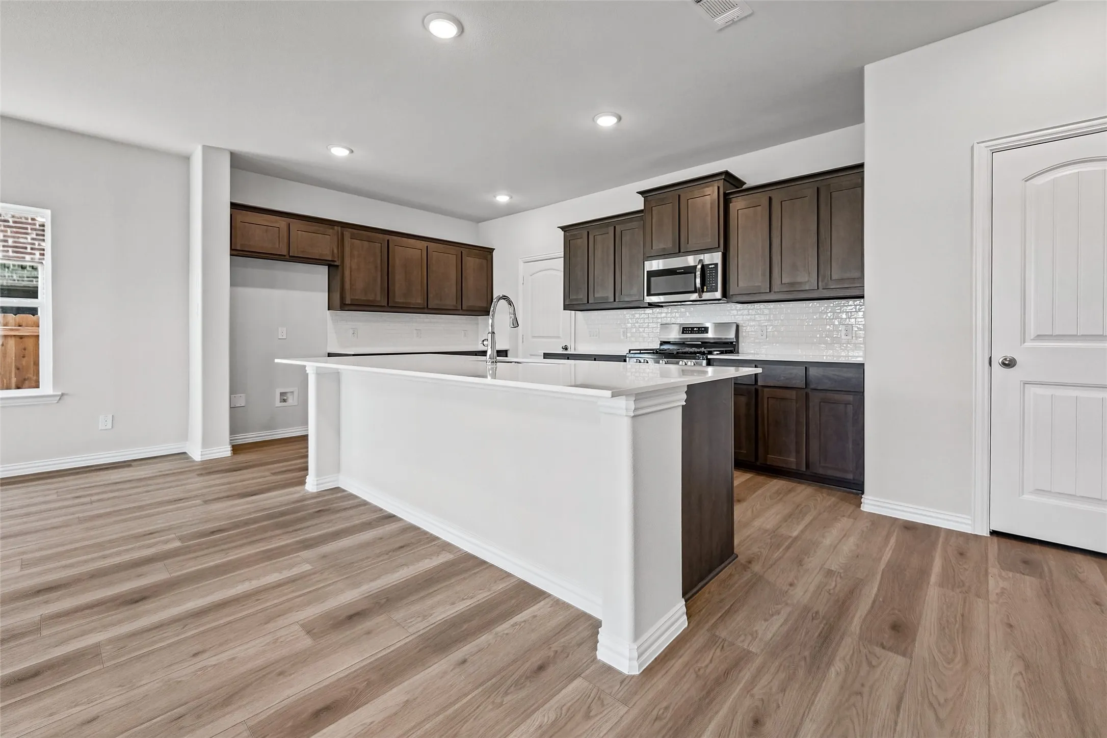 Kitchen featuring a central island, dark wood-finish cabinetry, white tile backsplash, and stainless steel appliances