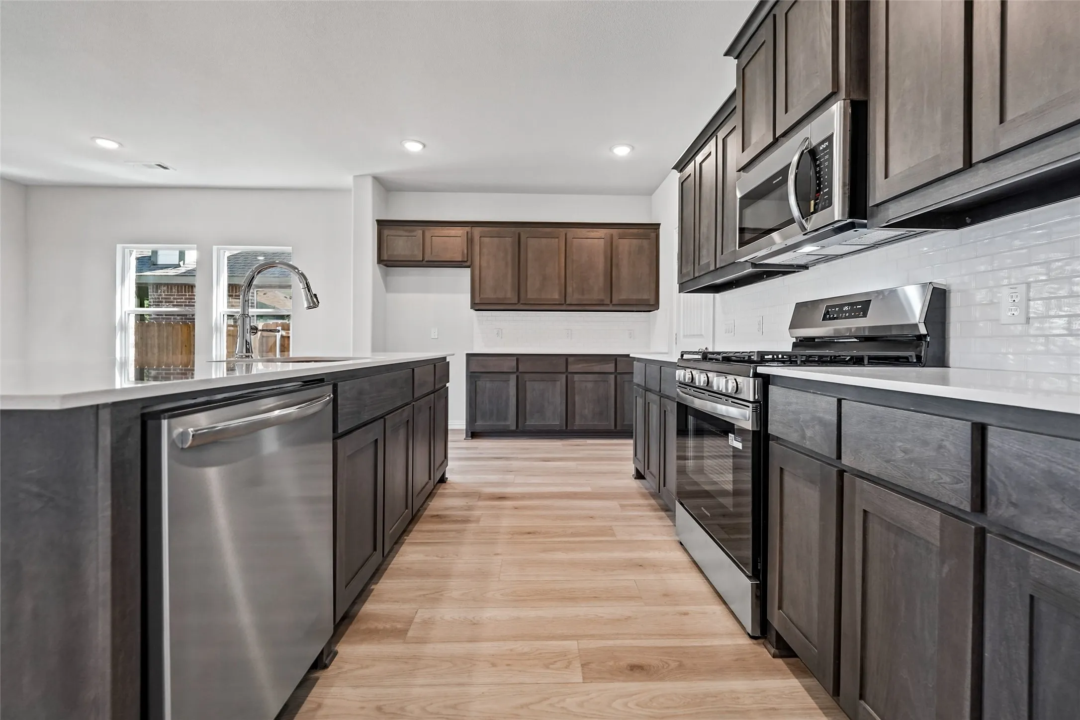 Modern kitchen with stainless steel appliances, dark wood-finish cabinetry, light countertops, and wood-finish flooring