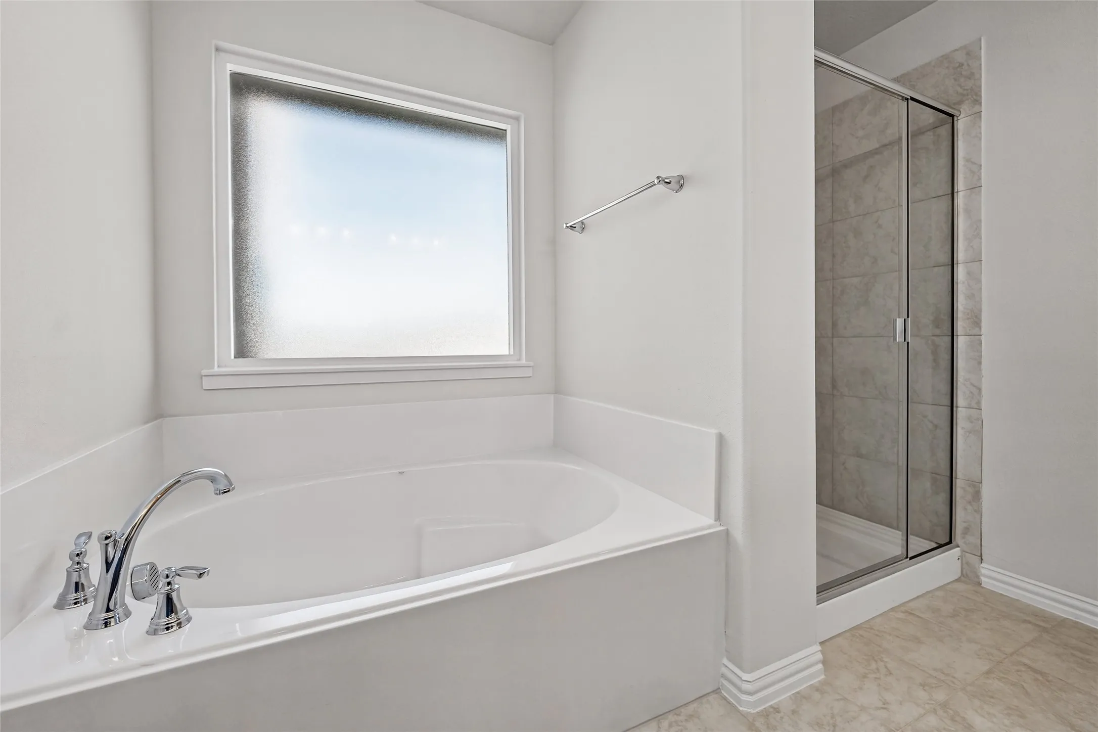 Recessed soaking tub with chrome fixtures, frosted window, and a separate glass-enclosed shower featuring tiled walls