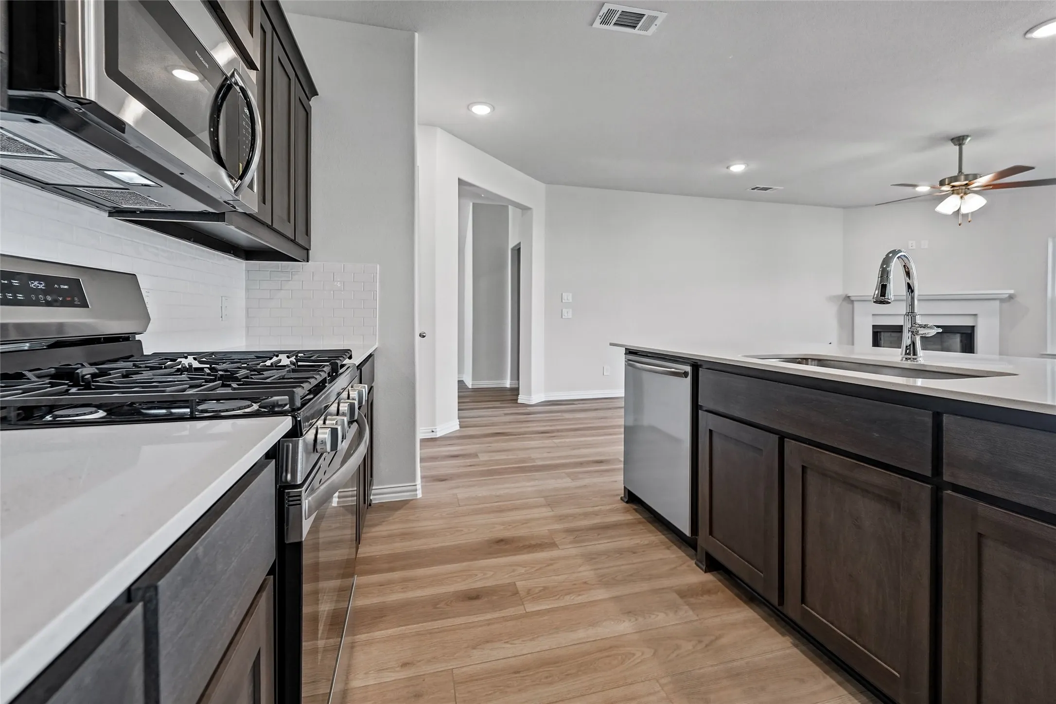 Kitchen featuring stainless steel appliances, white tile backsplash, light wood-finish flooring, dark cabinetry, and white countertops