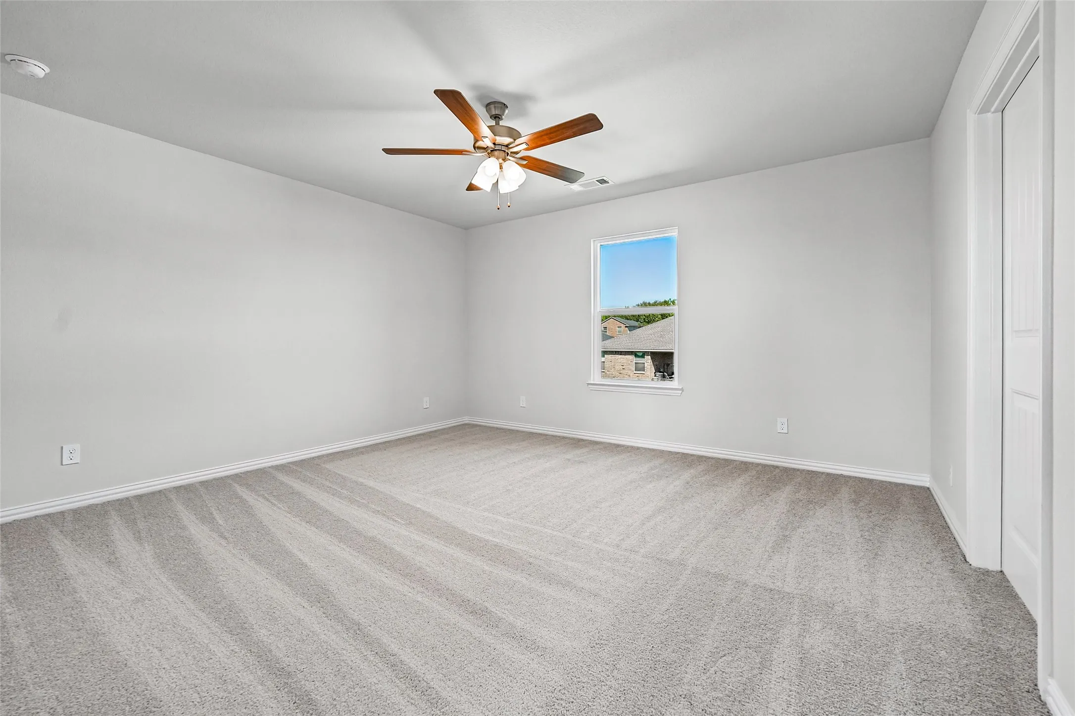 Spacious room featuring neutral carpeting, a ceiling fan with light, a single window, and a white paneled door