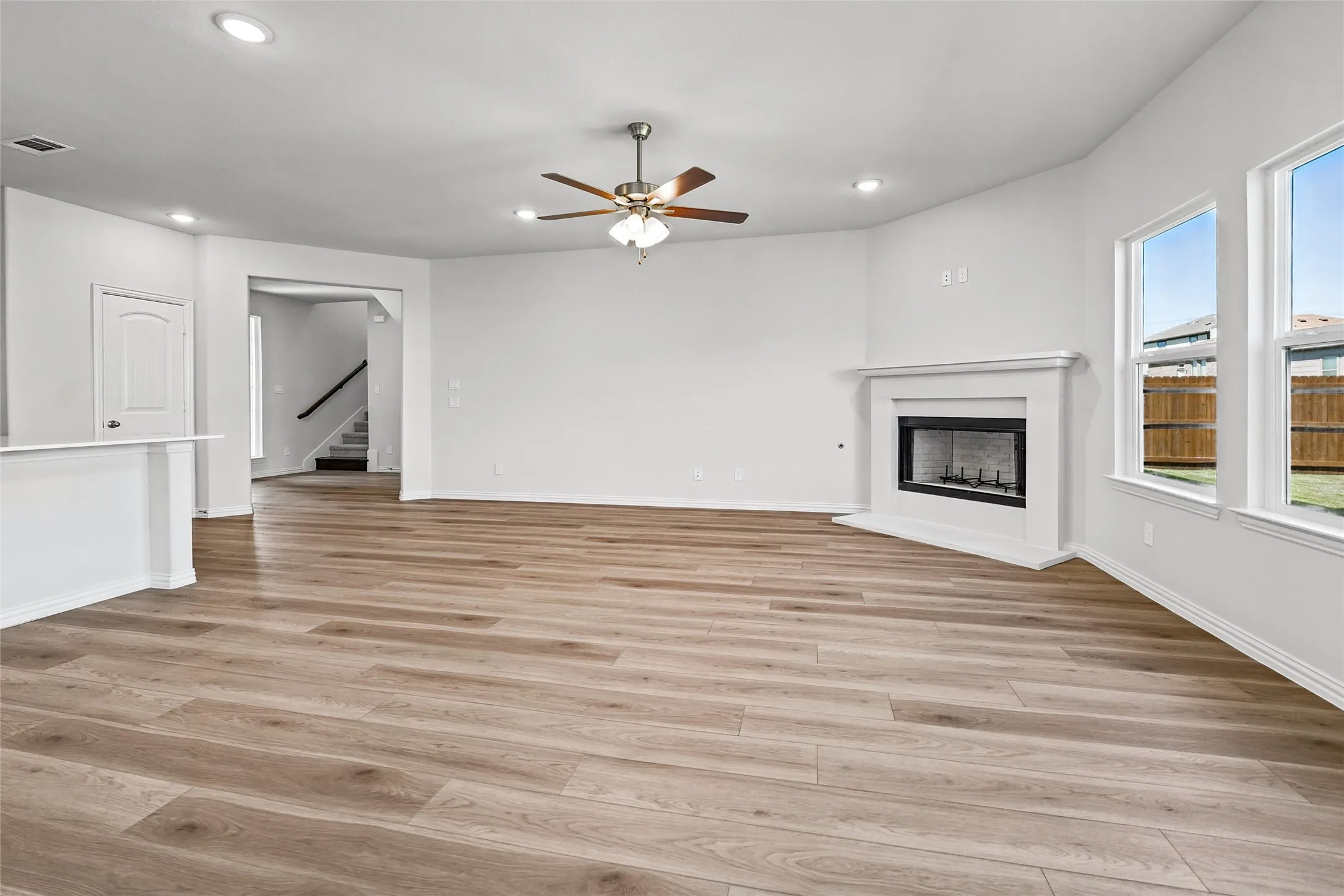 Spacious living area featuring wood-finish flooring, a decorative fireplace with a mantel, multiple windows, recessed lighting, and a ceiling fan