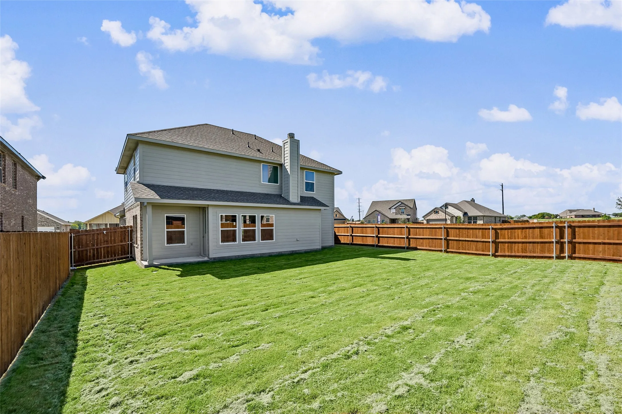 Expansive backyard featuring a manicured lawn, a full wood privacy fence, and a two-story residence with a light-colored exterior and multiple windows