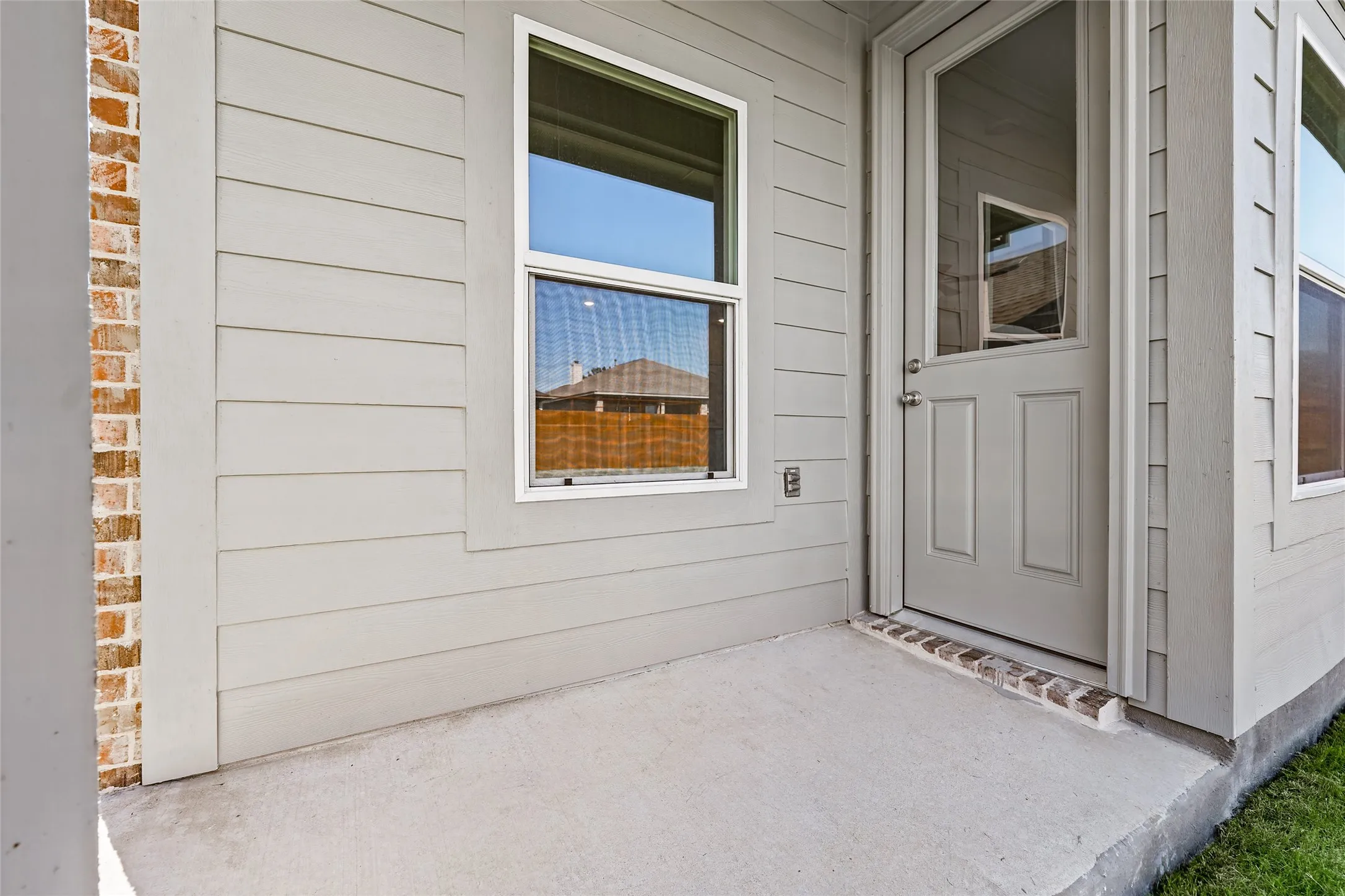 Concrete patio with a half-lite exterior door, light-colored siding, and brick accents