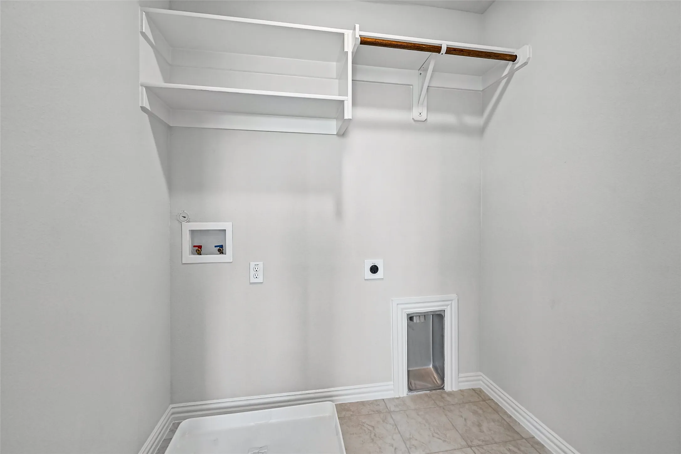 Laundry area with white shelving, a wood-finish hanging rod, and light-toned tile flooring
