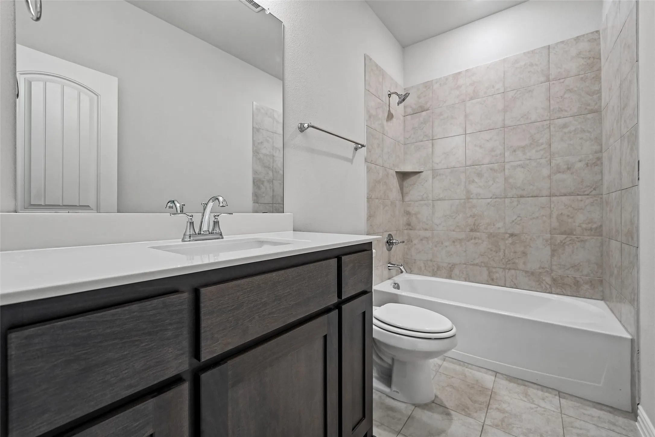 White bathtub with tiled surround, integrated shower niche, and a dark wood-finish vanity with a white countertop