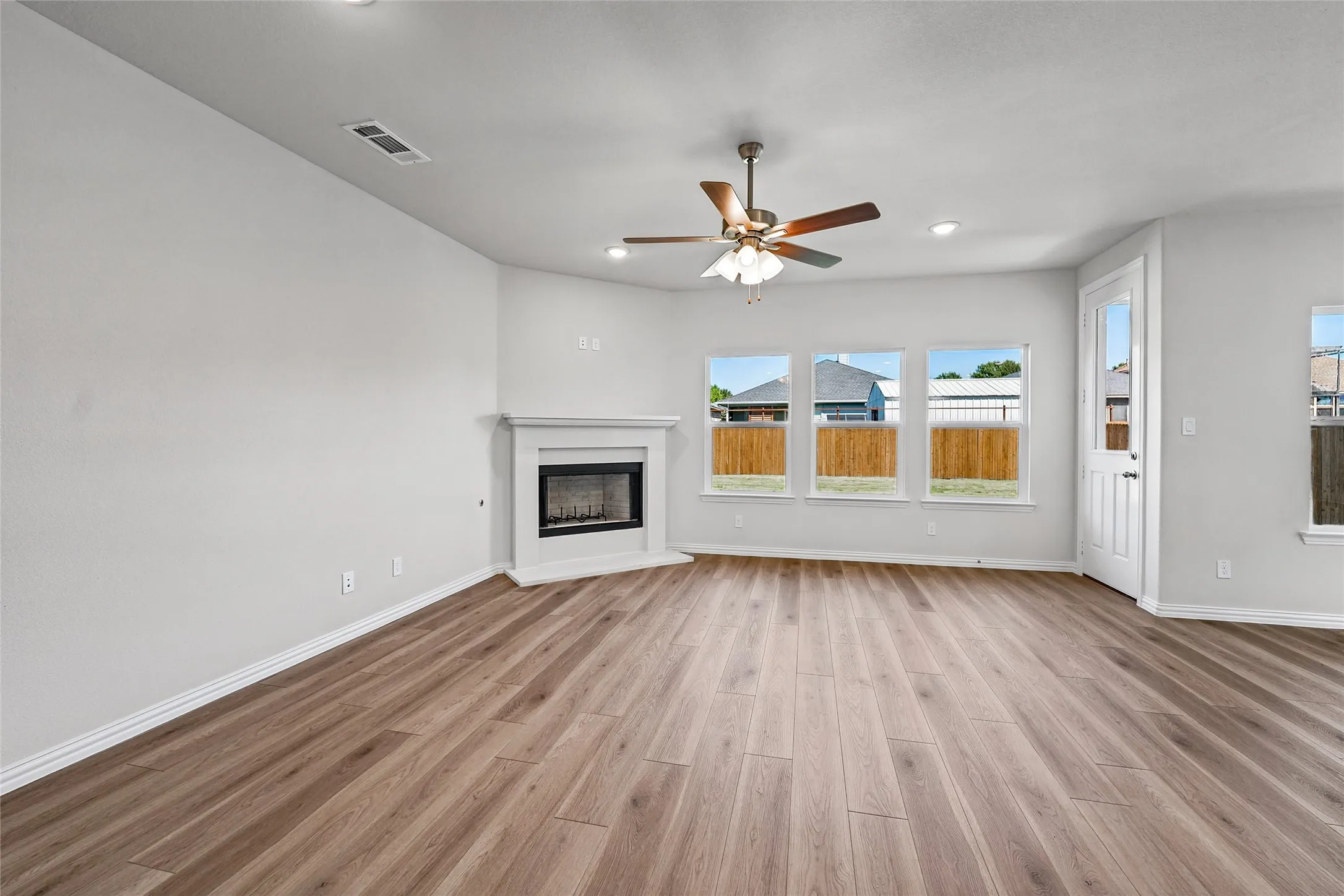 Wood-finish flooring, corner fireplace with white surround, ceiling fan, and multiple windows
