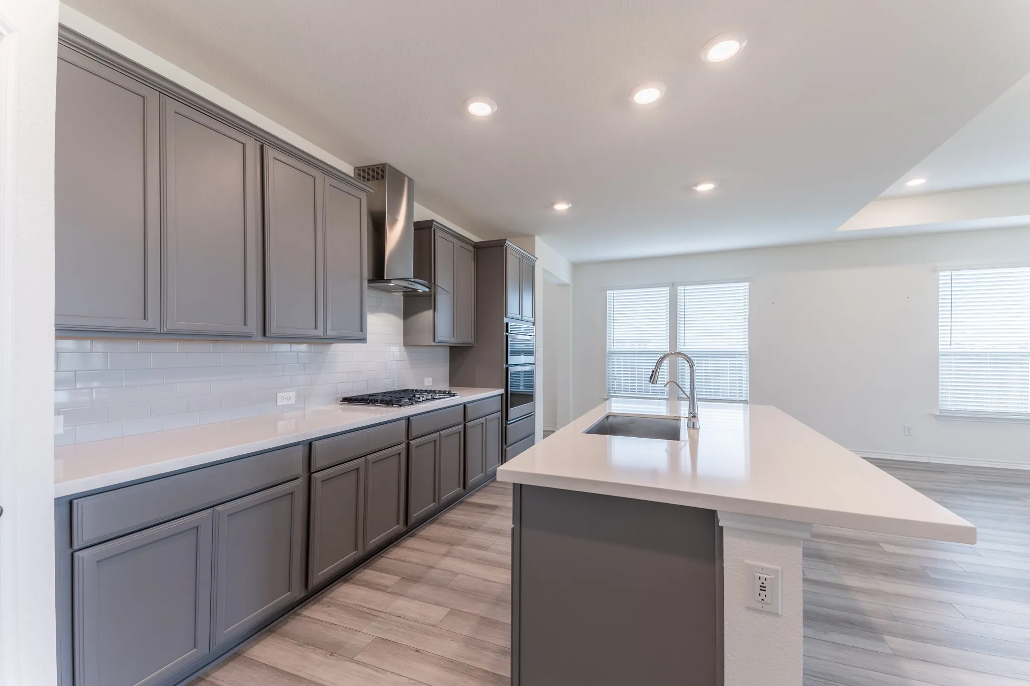 Kitchen featuring gray cabinetry, white quartz subway tile backsplash, white countertops, a gas cooktop with a stainless steel vent