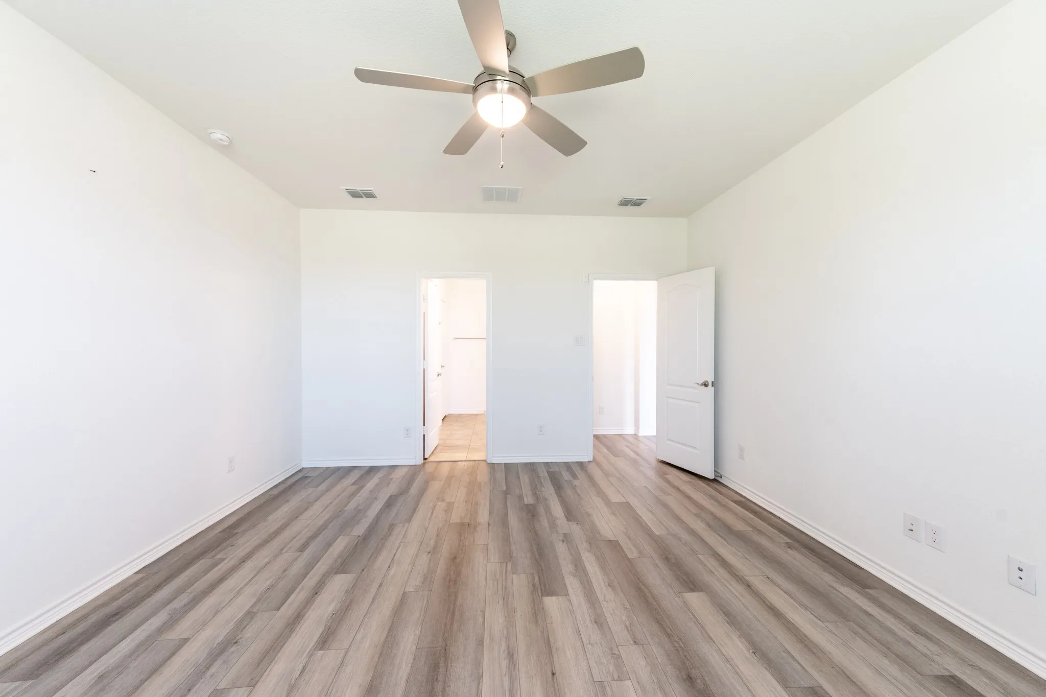 Spacious room featuring wood-finish flooring, white walls, and a ceiling fan with integrated lighting