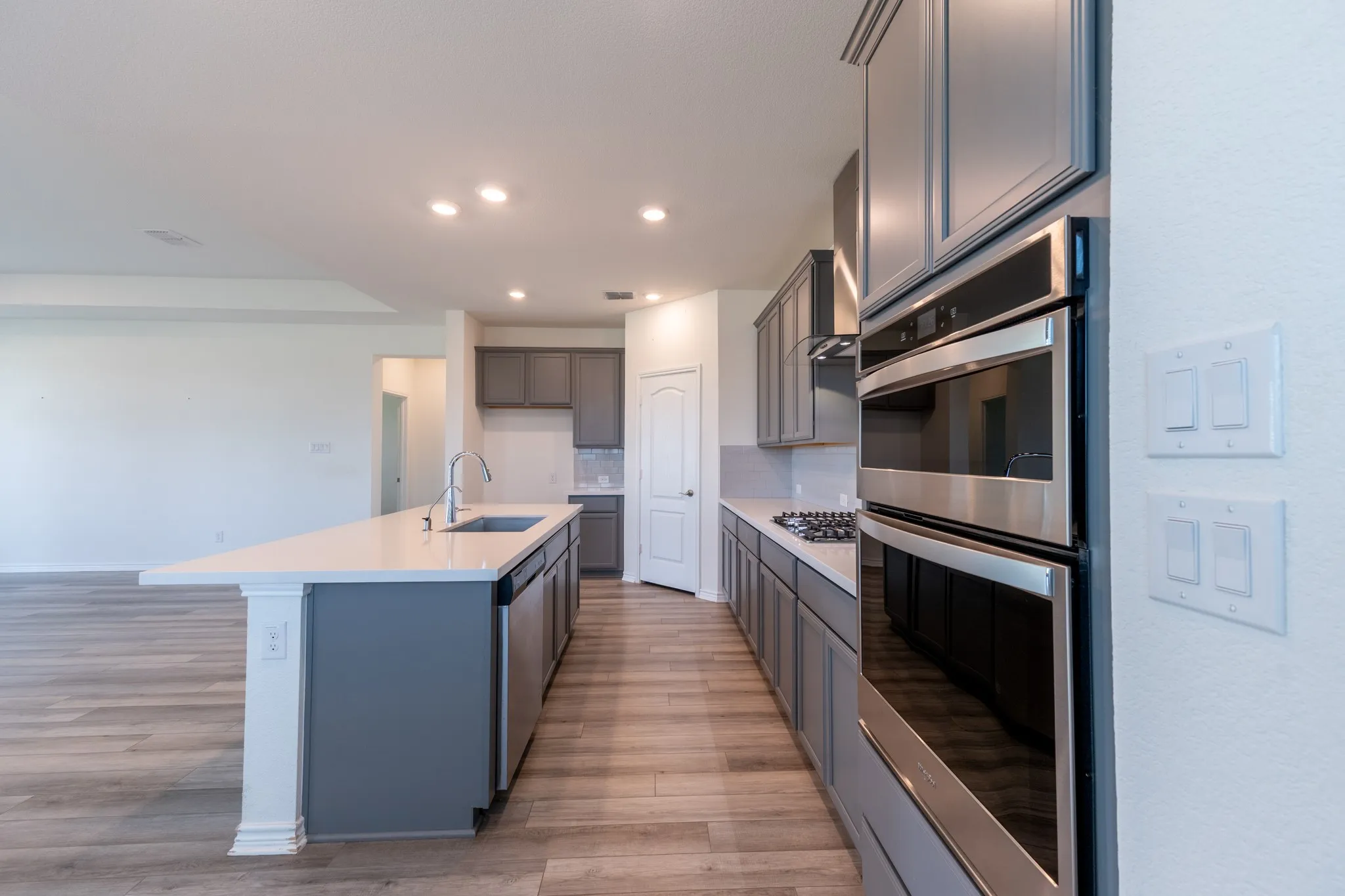 Kitchen featuring a large island, gas range, stainless steel range hood, subway tile backsplash, white quartz countertops