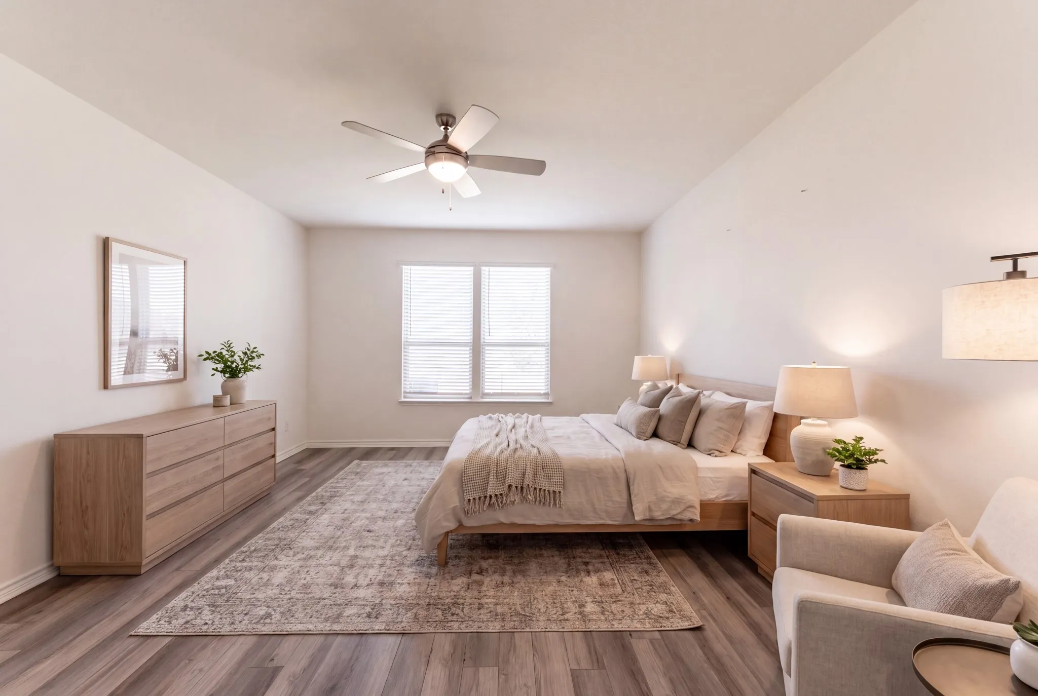 Virtually Staged: Primary bedroom suite featuring wood-finish flooring, a ceiling fan with integrated lighting, large windows with natural light, a wood dresser with mirror, and a seating area with upholstered furnishings and area rug accents