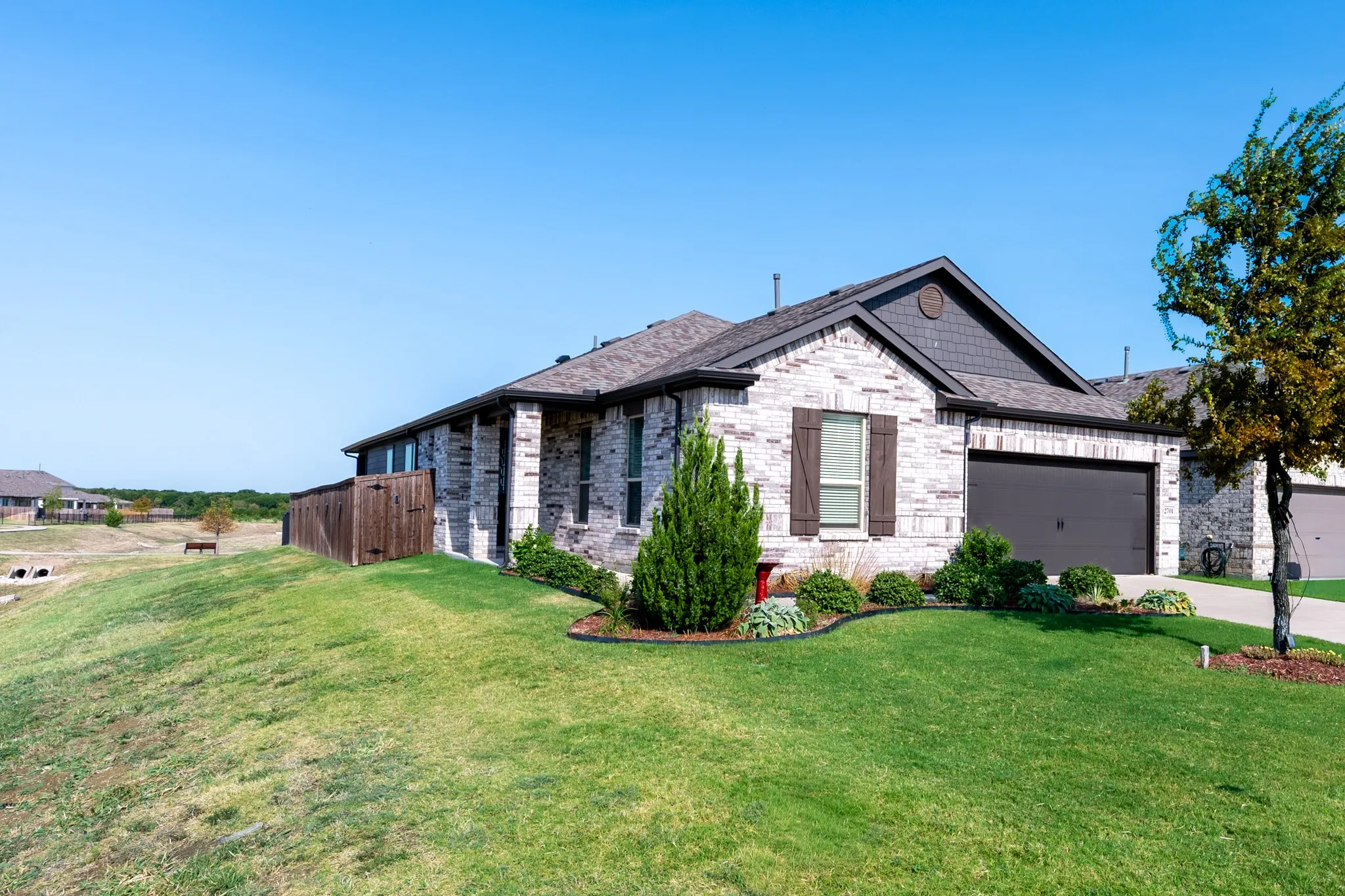 Brick exterior with dark gray siding accents, attached garage, well-maintained lawn, and mature landscaping