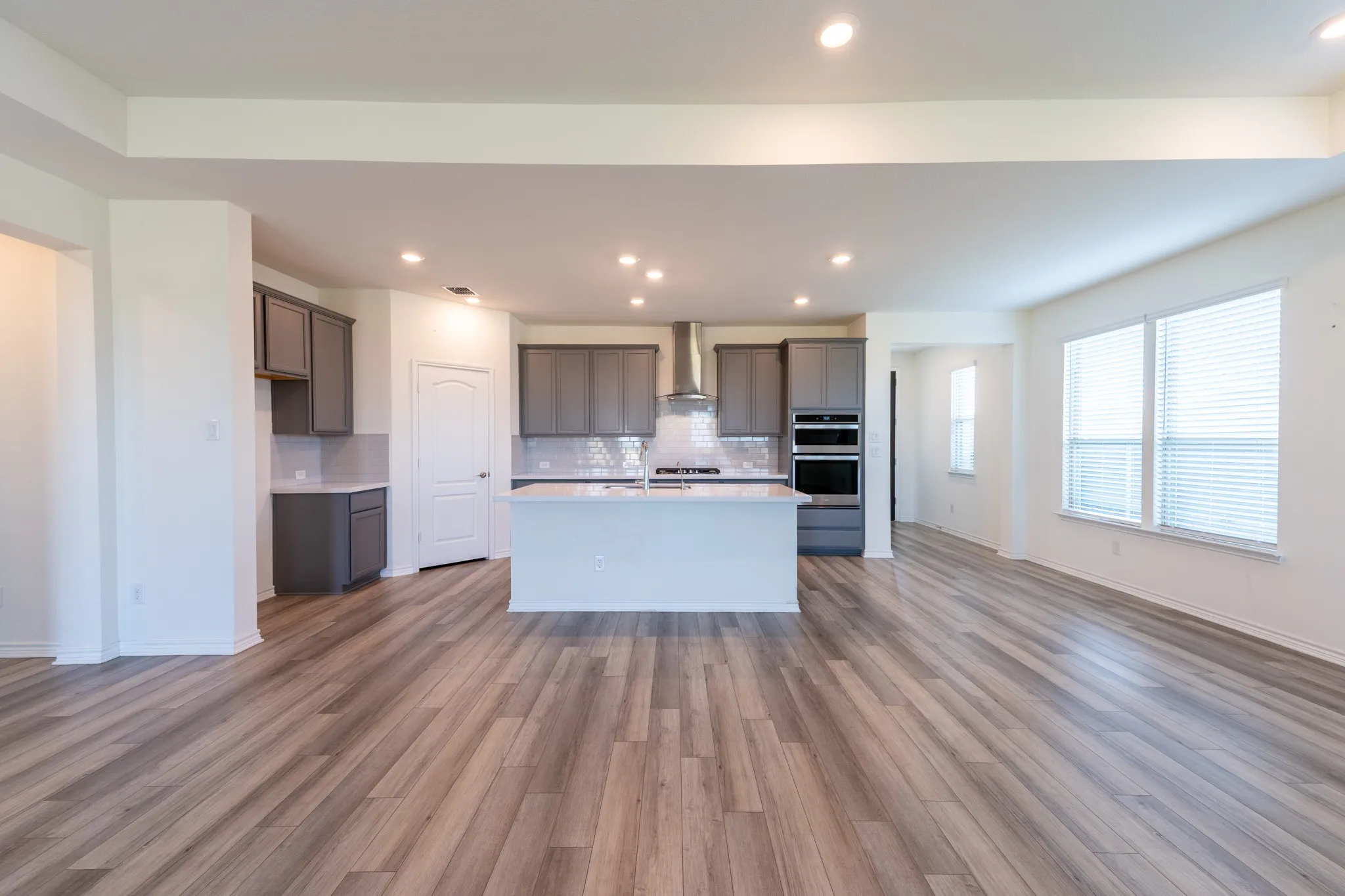 Open-concept living area featuring wood-finish flooring, recessed lighting, and a kitchen with an island, grey cabinetry, and built-in stainless steel appliances