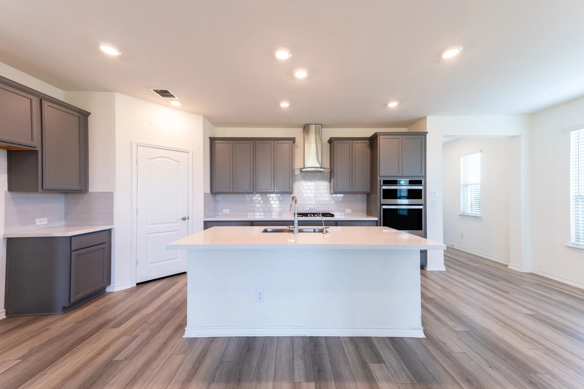 Kitchen featuring a large island,gas range, stainless steel range hood, subway tile backsplash, white quartz countertops