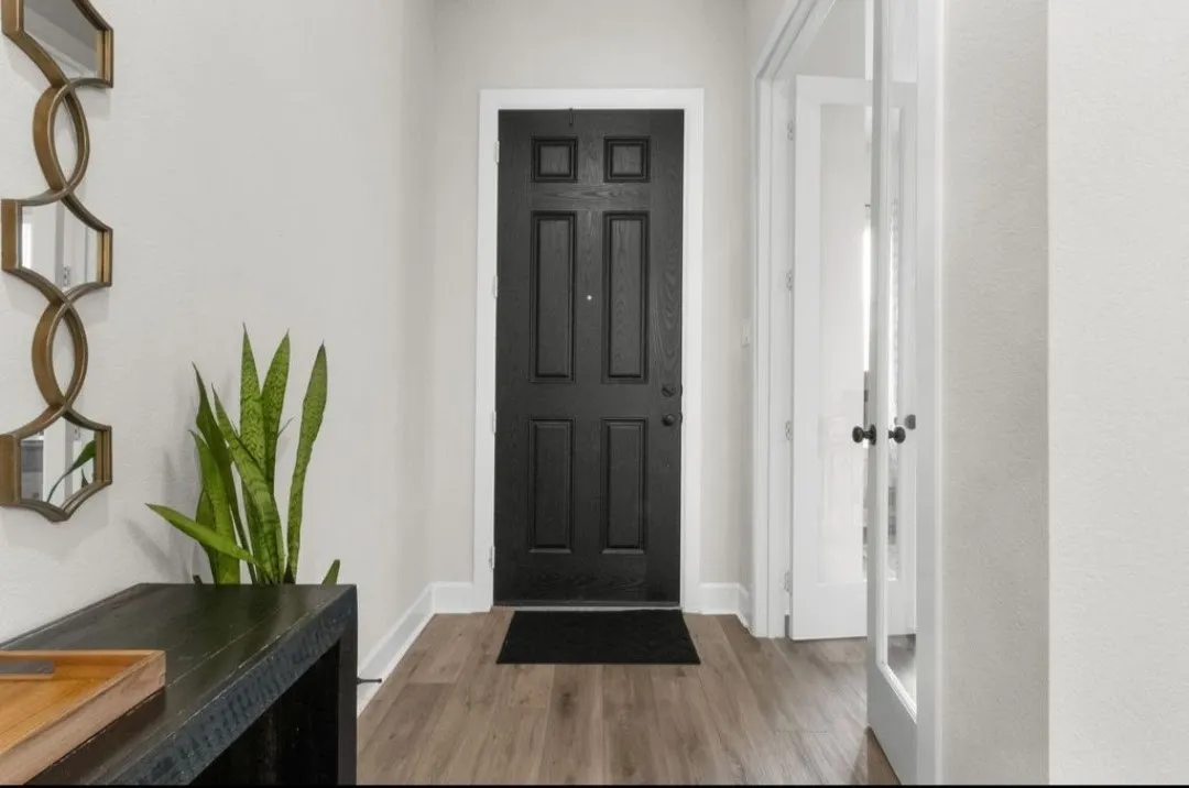 Panel front door with a matte finish, wood-finish flooring, and white interior walls