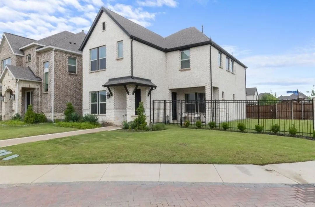 White brick exterior with dark trim, covered entry, black metal fencing, and a manicured lawn
