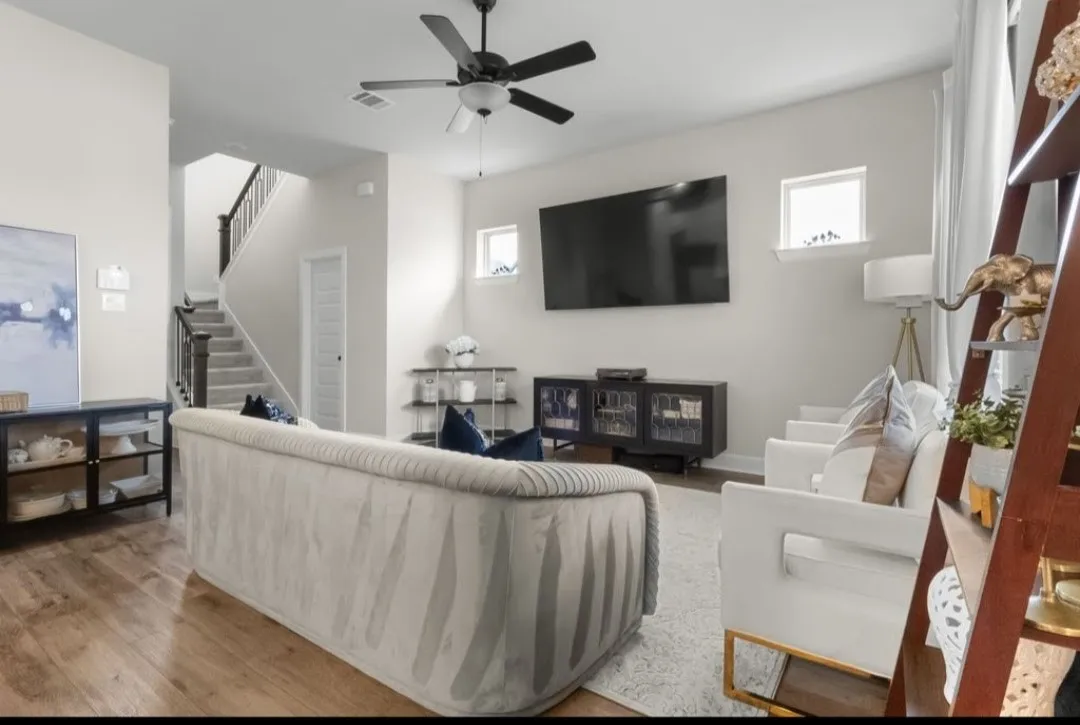 Spacious living area featuring wood-finish flooring, a ceiling fan, and a staircase with dark wood railings