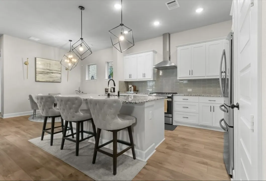 Open-concept kitchen featuring an island with a stone countertop, white cabinetry, stainless steel appliances, and wood-finish flooring
