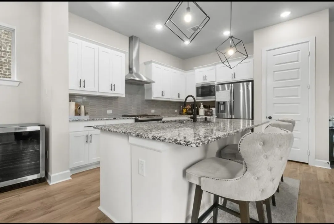 White cabinetry with dark hardware, stainless steel appliances, speckled stone countertops, gray subway tile backsplash, and wood-finish flooring