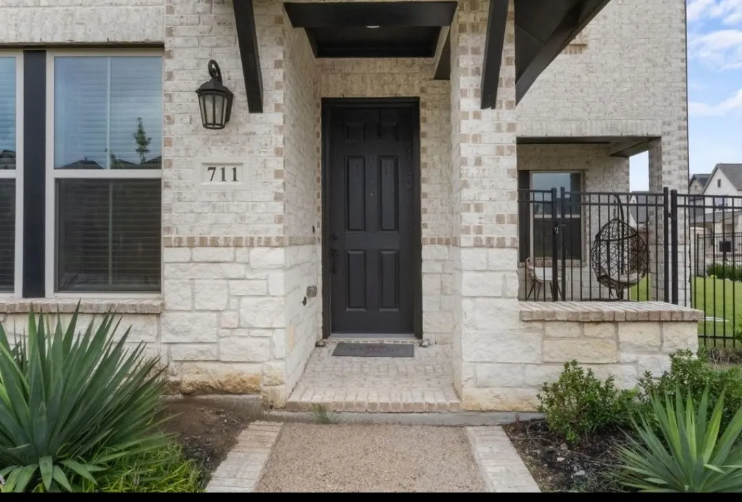 Stone and brick exterior with a prominent entryway, featuring a dark panel-style door, an ornamental outdoor light fixture, and an integrated covered porch area