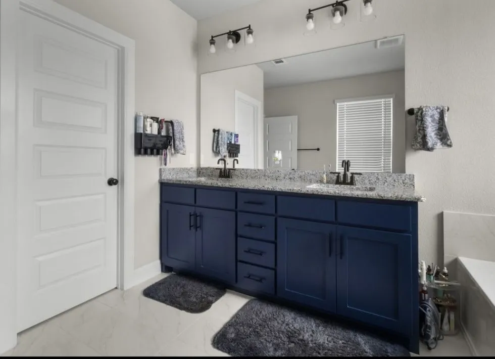 Double vanity with granite countertops, undermount sinks, matte black faucets, and dark blue cabinetry