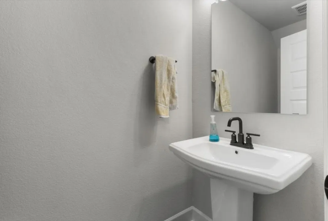 Pedestal sink with a matte black faucet, wall-mounted mirror, and a towel bar