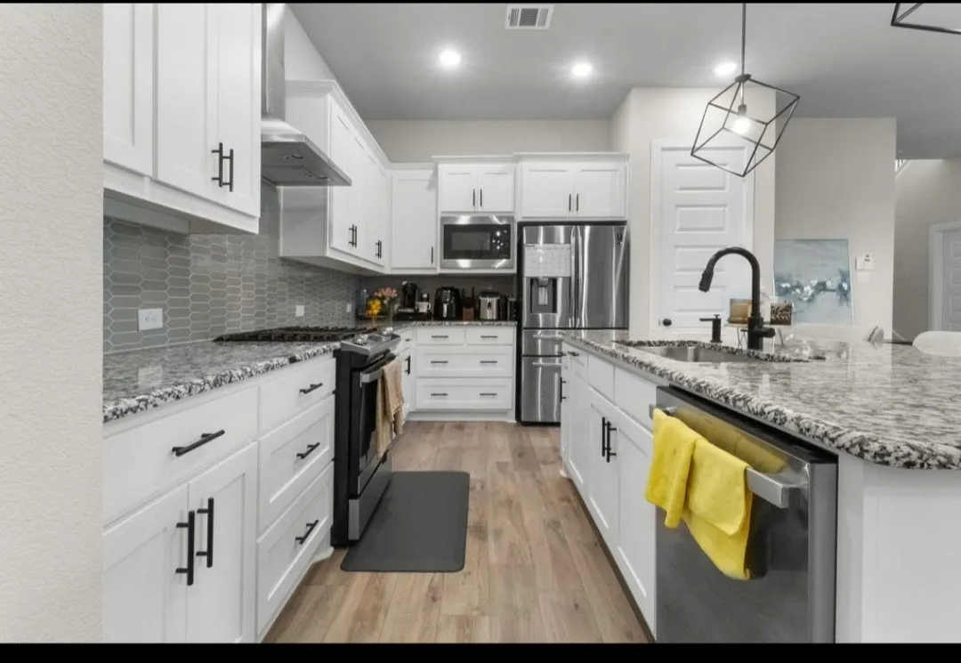 Modern kitchen featuring white cabinetry, stone countertops, stainless steel appliances, wood-finish flooring, and a decorative backsplash