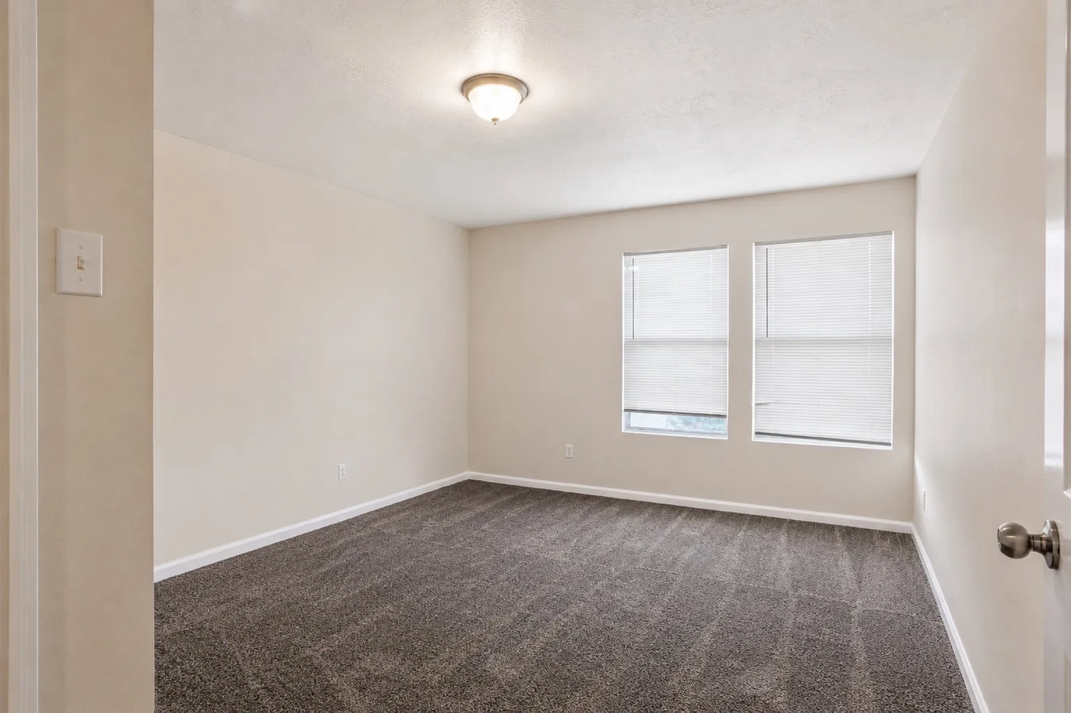 Neutral tone wall paint, textured ceiling, dark gray carpeting, and two windows