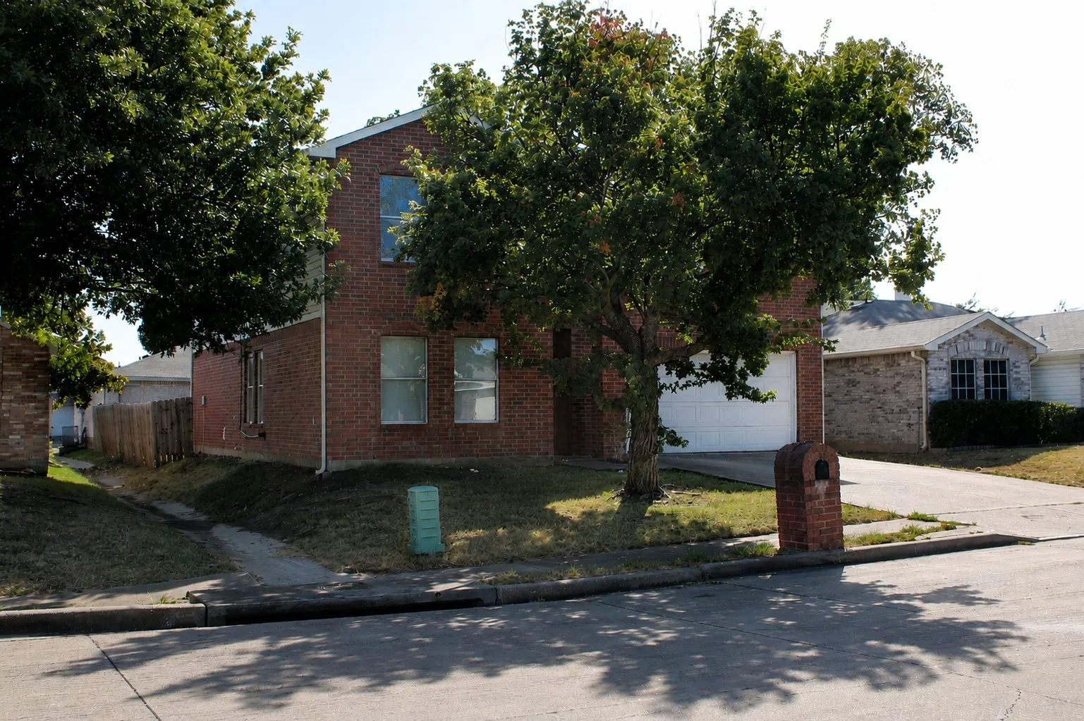 Brick exterior residence featuring an attached garage, a mature front yard tree, and a sidewalk entrance