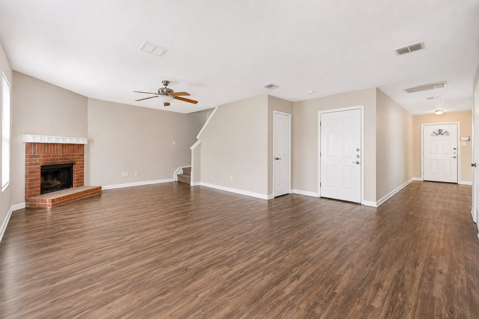 Spacious living area featuring wood-finish flooring, a brick fireplace with a white mantel, and a ceiling fan