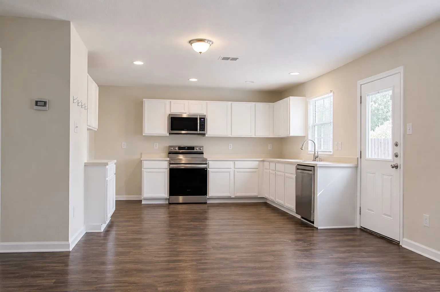 Open-concept kitchen with wood-finish flooring, white cabinetry, stainless steel appliances, and a window above the sink