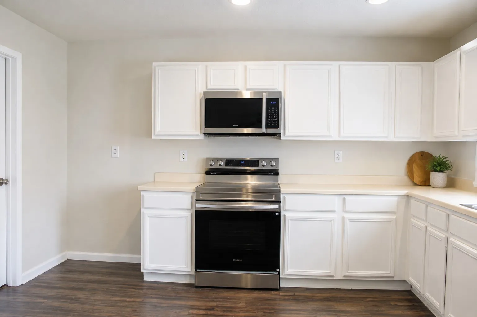 White cabinetry, stainless steel appliances, dark wood-finish flooring, light-toned countertops, and recessed lighting