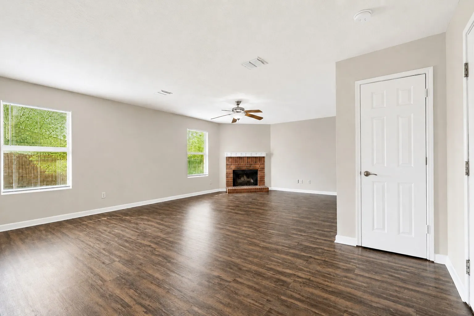 Spacious interior featuring wood-finish flooring, a brick fireplace, and multiple windows