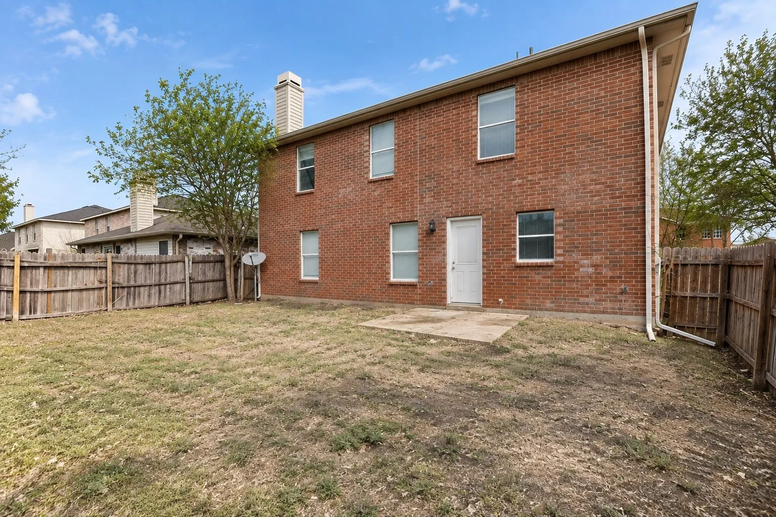 Brick exterior with multiple windows, a rear entry door, and a concrete patio