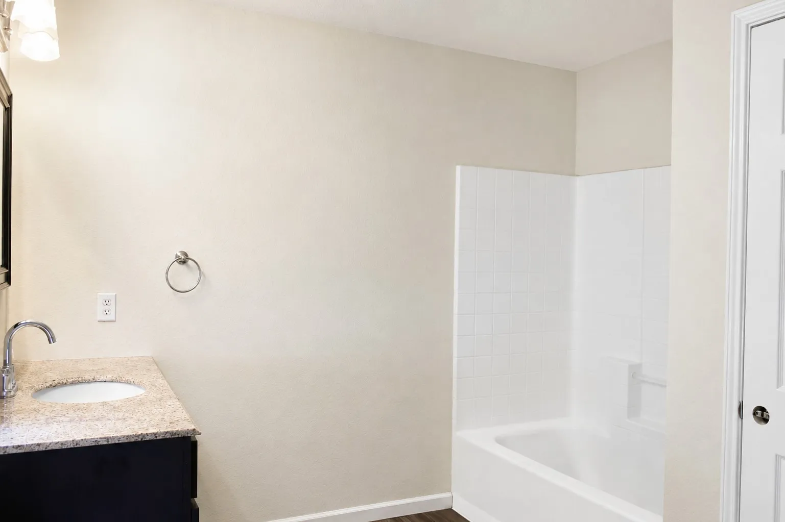 White bathtub with a tiled surround, dark wood-finish vanity, and a light-toned countertop