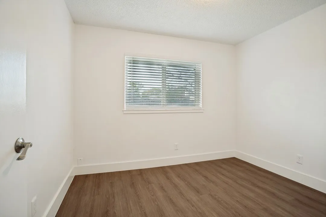 Wood-finish flooring, white wall paint, window with blinds, white trim, and a ceiling light fixture