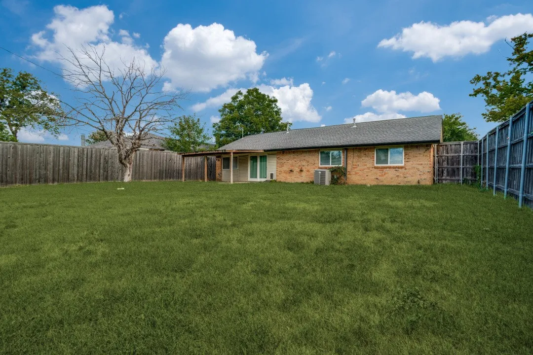 Expansive backyard featuring a manicured lawn, wood fencing, covered patio, and brick exterior