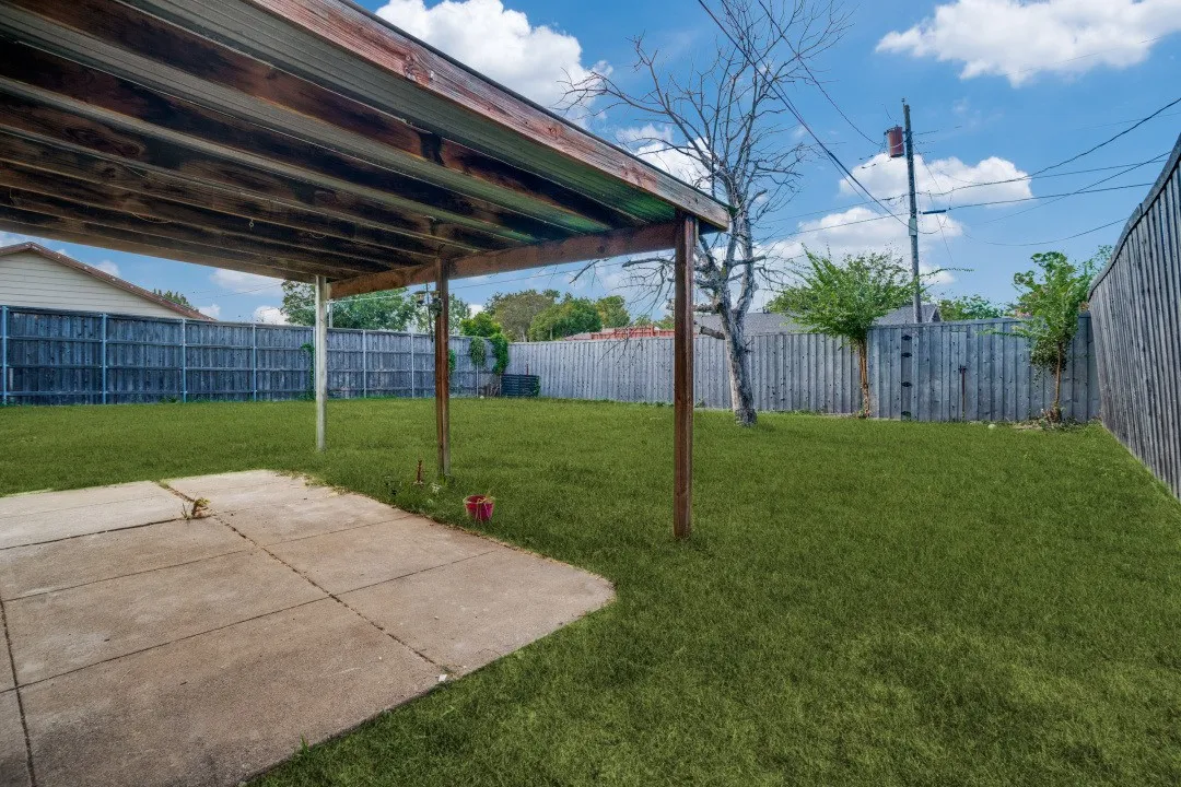 Expansive backyard with a covered patio, concrete slab, and wood privacy fencing