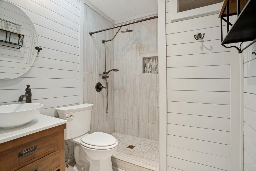 White shiplap walls complement the wood-finish vanity with a vessel sink